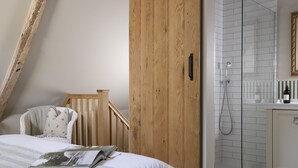 A bedroom with a wooden staircase, a bed with a magazine, a white bathroom with a glass shower enclosure, and a tiled floor. - Fabulously presented dog friendly holiday cottage with outside tub - The Coach House, South Cerney (South Cerney)
