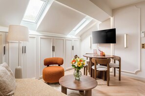 A modern living room with a high ceiling, skylight, a flat-screen TV, a round wooden table, a sofa, and a chair. - Merveil - Luxury Suite - Champs Elysees - St Cyr I (Paris)