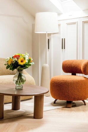 A modern living room with a round wooden coffee table, a vibrant orange armchair, and a vase of sunflowers. - Merveil - Luxury Suite - Champs Elysees - St Cyr I (Paris)