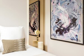 Ein Hotelzimmer mit einem Bett, einem Nachttisch mit Lampe sowie zwei abstrakten Bildern an der Wand.