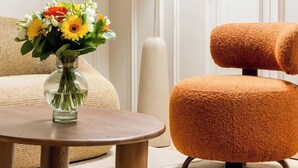 Een moderne woonkamer met een ronde houten salontafel, een opvallende oranje fauteuil en een vaas met zonnebloemen.