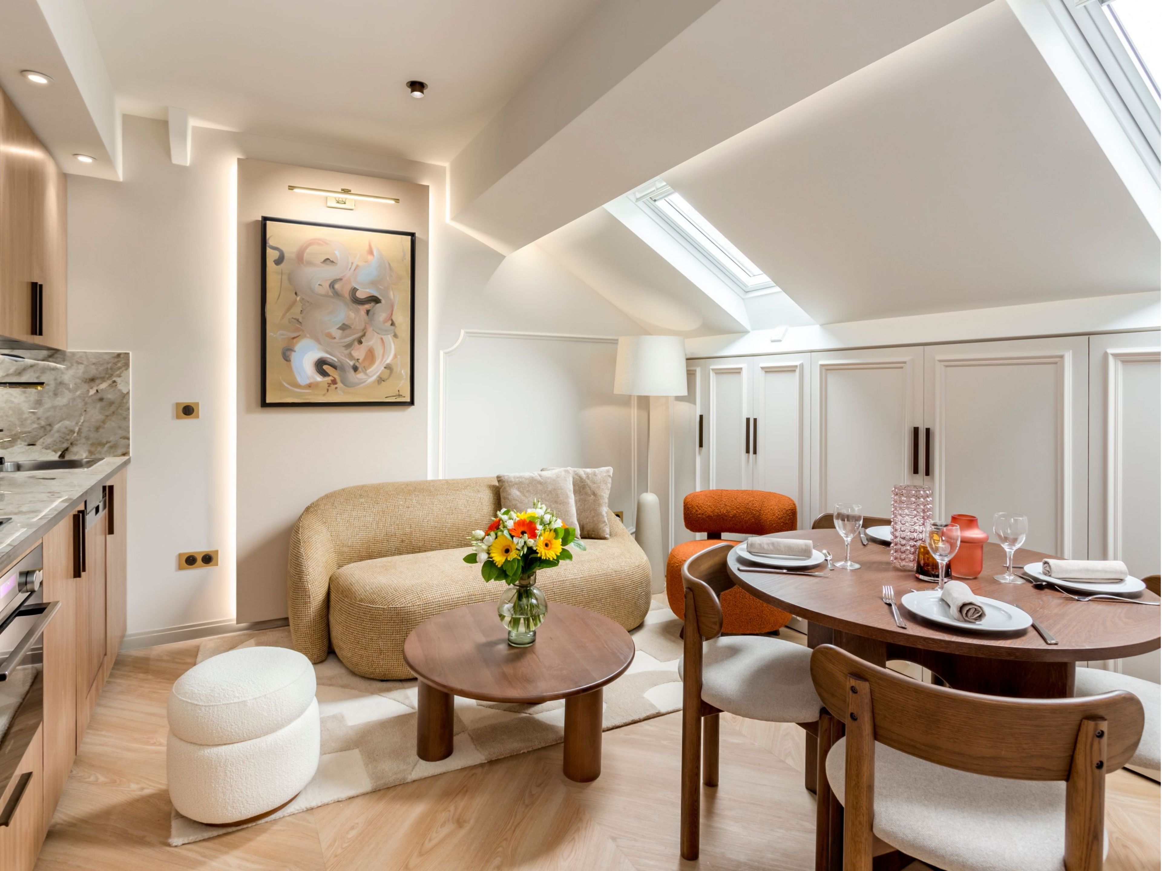 A modern dining area with a round table, wooden chairs, and a vase of flowers.