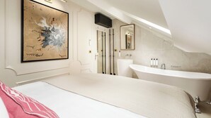 Een moderne badkamer met een groot bad, een wastafel en een spiegel. Op de muur hangt een lijst met een abstract schilderij en een deur met een zwarte handgreep.