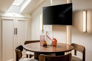 Ein Essbereich mit einem runden Holztisch, vier Stühlen, einem an der Wand befestigten Flachbildfernseher und einer dekorativen Vase auf dem Tisch.