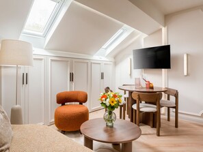 A modern living room with a sofa, ottoman, round coffee table, and a TV mounted on the wall. - Merveil - Luxury Suite - Champs Elysees - St Cyr I (Paris)