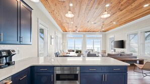A modern kitchen with dark blue cabinets, a large island with a built-in oven, and a wooden ceiling. - Cape San Blas Beach House - Starfish (Port St. Joe)