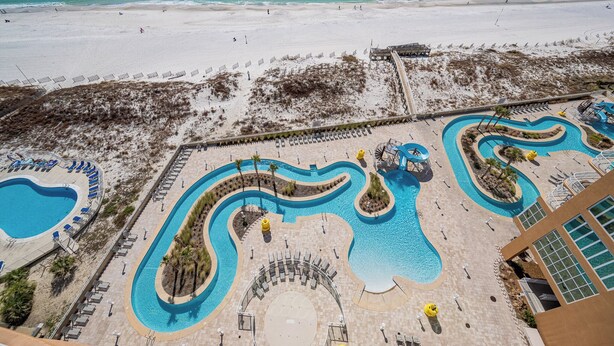 Ein Resort mit großem Poolbereich, einem Strand und einem Gebäude mit Meerblick.
