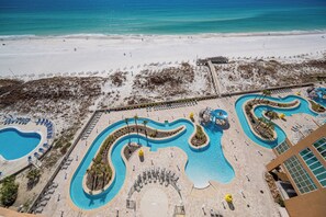 Un resort con un amplio espacio de piscina, una playa y un edificio con vista al océano.