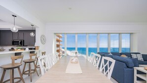 A modern kitchen with a view of the ocean, a dining area with a long table, and a blue sofa set. - Stunning Gulf views! - Phoenix Gulf Towers 1404 (Orange Beach)