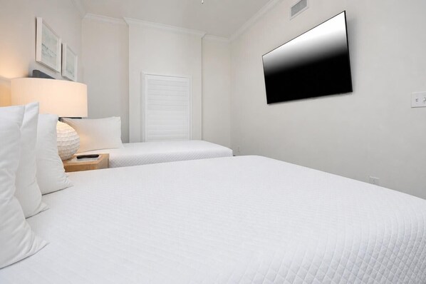 Habitación de hotel con dos camas, un televisor montado en la pared, una mesita de noche con lámpara y una puerta con ventanal.