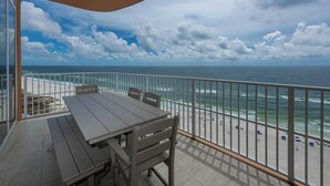 Ein Balkon mit Tisch und Stühlen mit Blick auf einen Strand mit Sonnenschirmen und Personen.