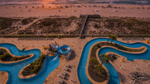 Ein Resort mit großzügigem Poolbereich, einer Rutsche und Blick auf den Strand.