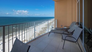 A balcony with a view of the beach and ocean. There are two chairs and a table on the balcony.