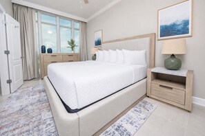 Un dormitorio con una cama grande, una mesita de noche, una lámpara, una ventana con cortinas y una puerta.