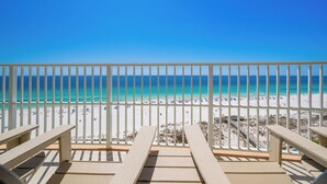 A beach view from a balcony with a railing, beach chairs, and a clear blue sky.