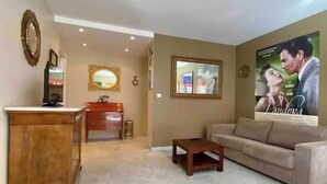 Una sala de estar con un sofá color beige, una mesa de centro de madera, un armario de madera, un espejo y un cartel en la pared.