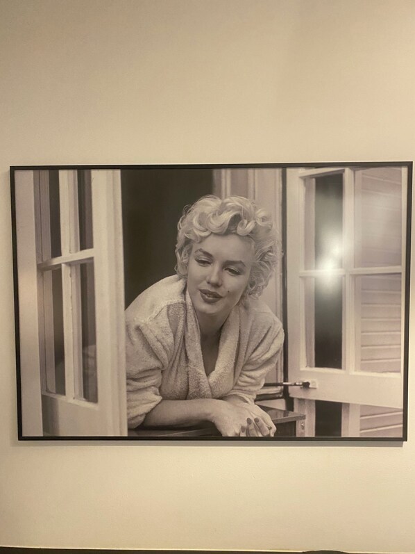 A framed black and white photograph of a person leaning out of a window with white trim and a dark interior.