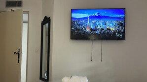 Habitación de hotel con cama, televisión de pantalla plana mostrando un paisaje urbano, espejo y puerta.