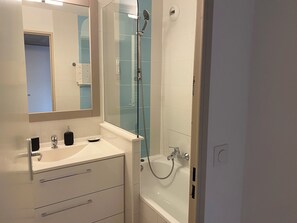 A modern bathroom with a glass-enclosed shower, a white sink with a mirror, and a white bathtub.
