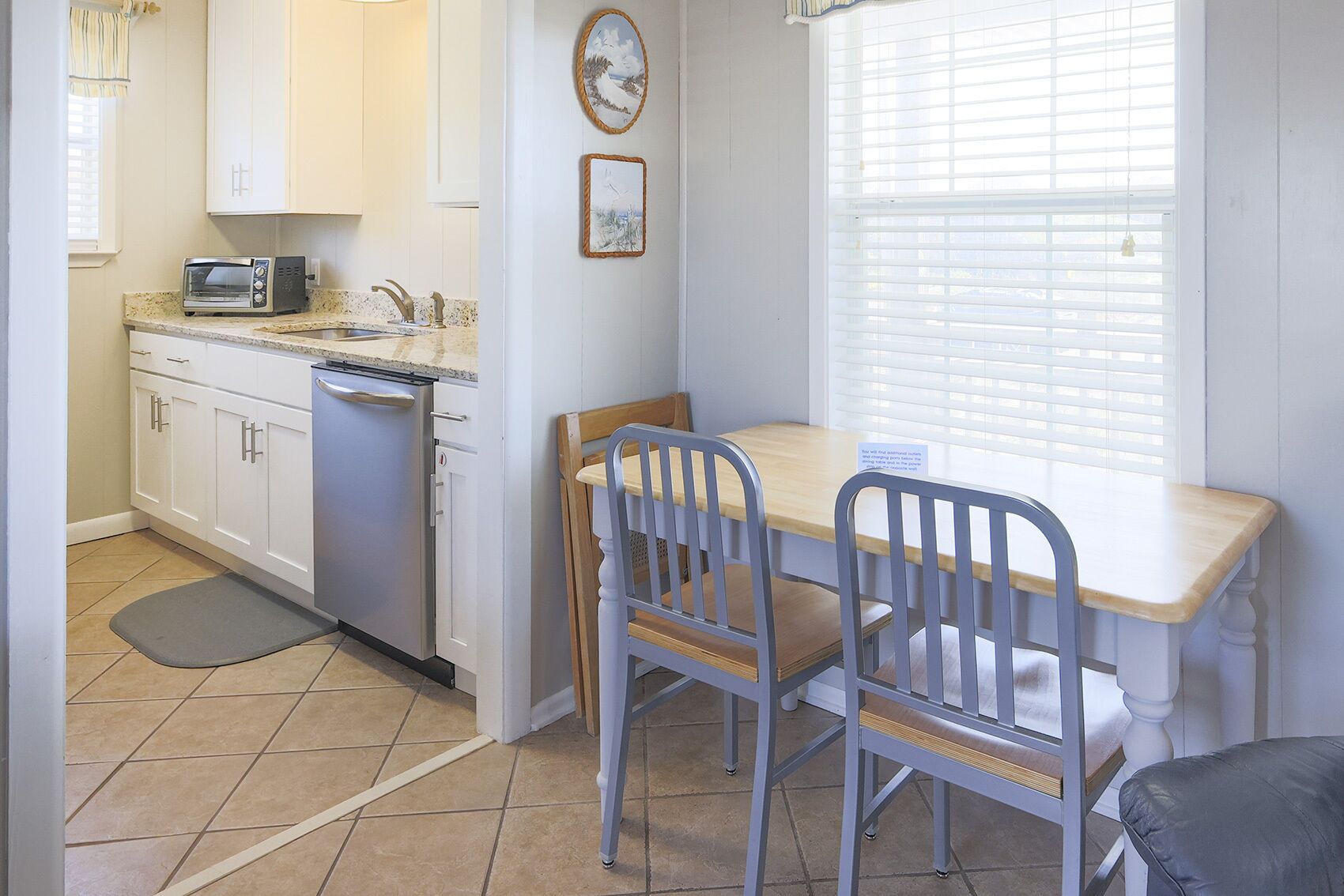 A compact kitchen with white cabinets, a microwave, and a sink. There is a dining table with two chairs and a small rug on the floor.