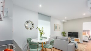 Un salon moderne avec un canapé gris, un téléviseur et un coin repas comprenant une table ronde et des chaises.