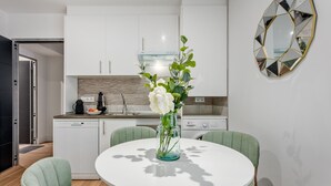 Une cuisine moderne avec des meubles blancs, un four encastré et une machine à café. On y trouve une table à manger avec des chaises et un vase de fleurs.