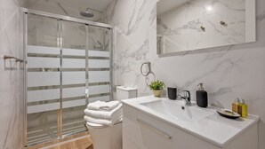 A modern bathroom with a glass shower enclosure, a white sink with a marble countertop, and a large mirror above the sink. - Modern 2-Bed Apartment Near Bernabéu (Madrid)