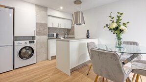A modern kitchen with a built-in washing machine, a central island, and a dining area with a glass table and chairs. - Modern 2-Bed Apartment Near Bernabéu (Madrid)