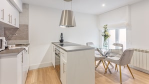 A modern kitchen with white cabinetry, a built-in oven, and a glass dining table with chairs. - Modern 2-Bed Apartment Near Bernabéu (Madrid)