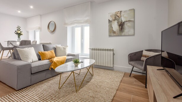 A modern living room with a grey sofa, a round coffee table, and a grey armchair. - Modern 2-Bed Apartment Near Bernabéu (Madrid)