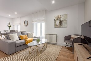A modern living room with a grey sofa, a round coffee table, and a grey armchair. - Modern 2-Bed Apartment Near Bernabéu (Madrid)