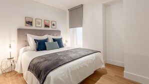 A modern bedroom with a large bed, a bedside table with a lamp, and a window with a blind. - Modern 2-Bed Apartment Near Bernabéu (Madrid)