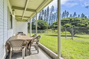 Un porche cubierto con una mesa y sillas, con vista a un patio cercado con árboles.