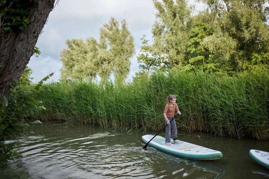 Una persona fa paddleboard su un fiume tranquillo, circondata da una vegetazione lussureggiante e alberi.