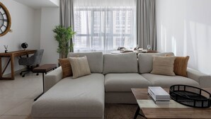 A modern living room with a sectional sofa, a wooden coffee table, a desk with a chair, and a large window with curtains. - Handsome 1BR in Armada Tower 3 (Dubai)