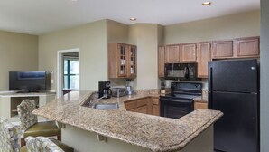 A kitchen with granite countertops, wooden cabinets, a black refrigerator, and a microwave. There is a dining area with a TV and chairs. - 3Bed/2Bath Deluxe Unit, Smoky Mountains!  (Sevierville)