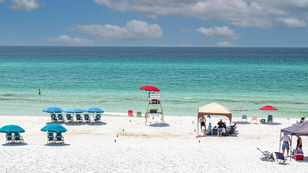 Une plage de sable blanc, avec une eau turquoise et limpide, et quelques parasols qui offrent de l’ombre.