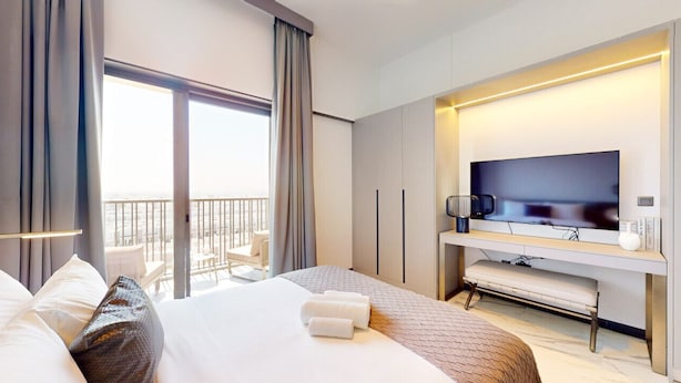 A hotel room with a large bed, a flat-screen TV, a desk with a chair, and a balcony with a view. - Meydan Studio | Skyline View, 12 Mins to Downtown I Mag Eye 910 (Meydan)