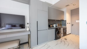 A modern kitchen with grey cabinetry, a built-in oven, a washing machine, and a flat-screen TV. - Meydan Studio | Skyline View, 12 Mins to Downtown I Mag Eye 910 (Meydan)
