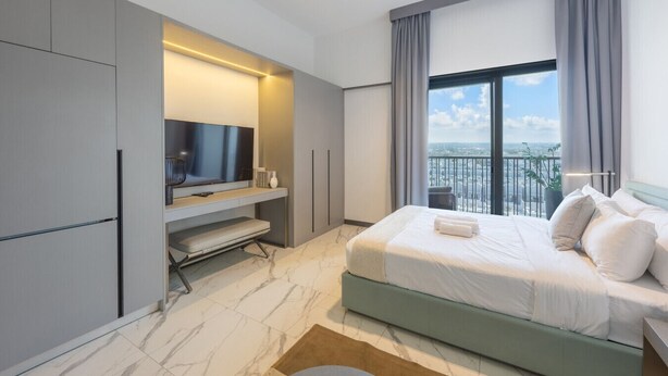 A modern hotel room with a large bed, a flat-screen TV, a seating area, and a balcony with a city view.