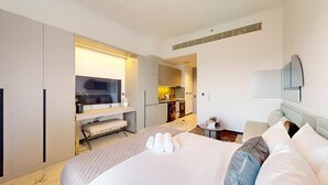 A hotel room with a bed, a TV, a kitchenette, and a bathroom.