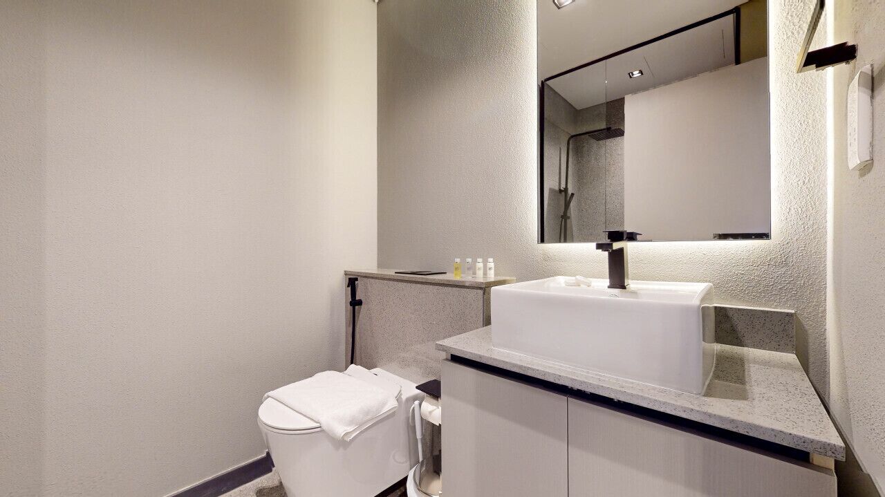Une salle de bain moderne avec un lavabo, un miroir et des toilettes, le tout de couleur blanche.
