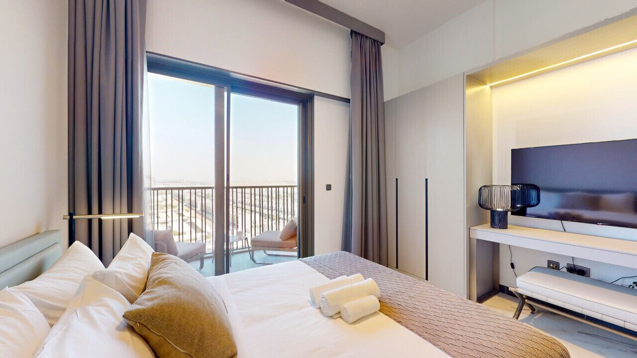 A hotel room with a bed, a TV, a balcony, and curtains.