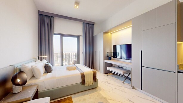 A modern bedroom with a large bed, a TV, and a desk area. - Mag Eye 920 - Classy Studio Apartment in Meydan (Meydan)