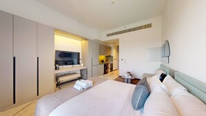 Moderni hotellihuone, jossa on suuri sänky, televisio, pieni keittiö ja kylpyhuone.