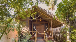 A wooden house with a thatched roof, surrounded by lush greenery and bamboo. - Pousada Castelo do Vento (Cruz)