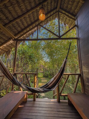 A hammock under a thatched roof structure with wooden benches and a view of a garden path. - Pousada Castelo do Vento (Cruz)