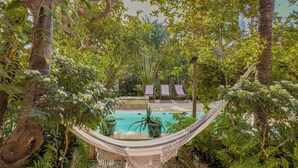 A hammock over a pool, surrounded by lush greenery and a thatched roof. - Pousada Castelo do Vento (Cruz)
