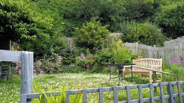 Un jardin avec un banc en bois, une table en métal et une variété de plantes et de fleurs.