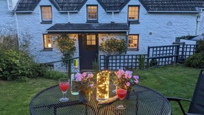 A table set outdoors with drinks and a decorative centerpiece, a house with a white exterior and dark roof in the background.